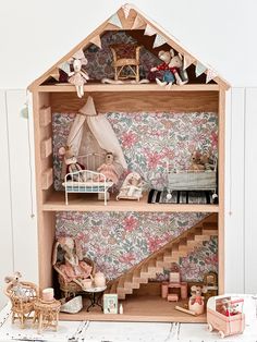 a doll house with furniture and accessories on the floor in front of a floral wallpapered wall