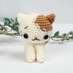 a small crocheted cat sitting on top of a white table next to green leaves