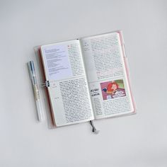 an open book with a pen sitting on top of it next to a white surface