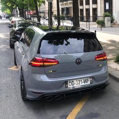 the rear end of a silver volkswagen car parked in a parking lot next to trees