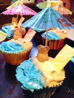 cupcakes decorated with blue frosting and colorful umbrellas are sitting on a table