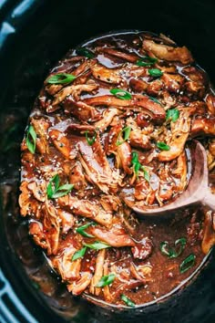 slow cooker filled with meat and vegetables being stirred by a wooden spoon in it