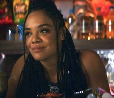 a woman with dreadlocks sitting at a table in front of some bottles and glasses