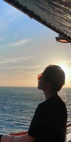 a person sitting on a boat looking out at the ocean with sun in the distance