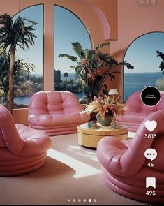 a living room filled with pink furniture next to large windows and palm trees in the background