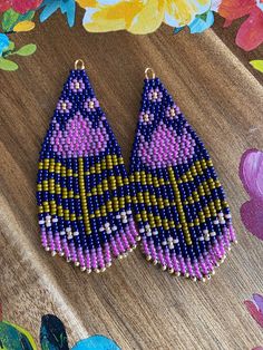 two pairs of beaded earrings sitting on top of a wooden table next to flowers