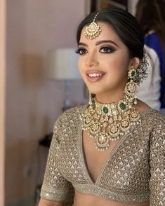 a woman in a gold and green bridal outfit with jewelry on her neck, smiling at the camera