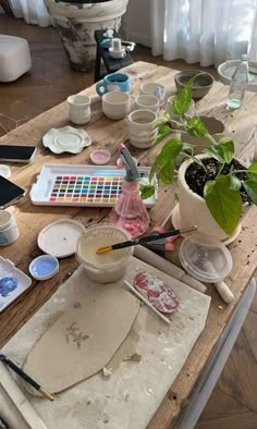 a wooden table topped with lots of crafting supplies and pots filled with plant life