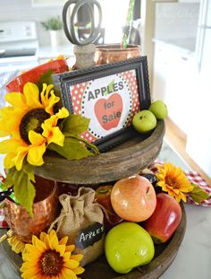 apples and sunflowers are arranged on a three tiered tray with an apple sign