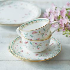 three tea cups and saucers sitting on top of each other with pink flowers in the background