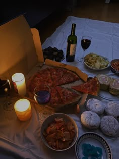 a table topped with pizza and other foods next to wine glasses on top of a white cloth