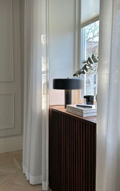 a table with a lamp and some books on top of it next to a window