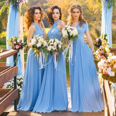 three bridesmaids in blue dresses stand under an arch decorated with flowers and greenery