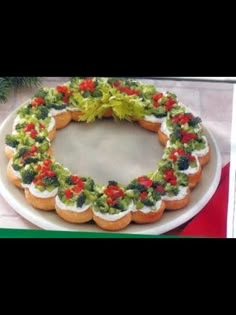 a christmas wreath shaped cake on a white platter with red and green toppings