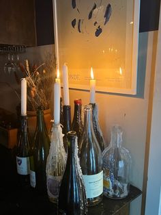 wine bottles and candles are sitting on a table in front of a framed art piece