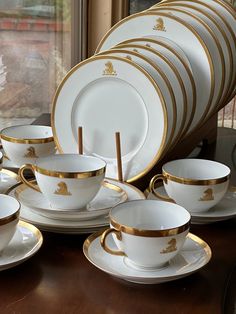 a table topped with lots of white and gold cups and saucer set next to a window