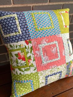 a colorful pillow sitting on top of a wooden bench next to a brick wall with a green and red patchwork design