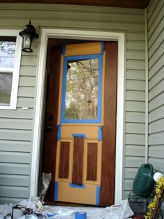 a cat sitting in front of a door that has been painted blue and yellow with brown trim