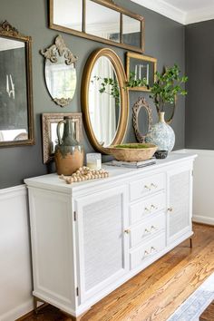 a white dresser with mirrors and vases on top