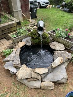 a water fountain in the middle of a garden with rocks around it and flowers on either side