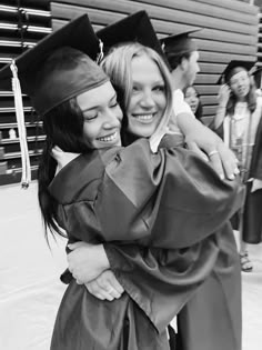 two women hugging each other in graduation gowns and caps at the end of a ceremony