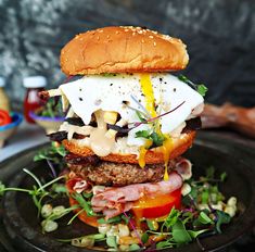 a burger with cheese, lettuce, tomato and other toppings sits on a black plate