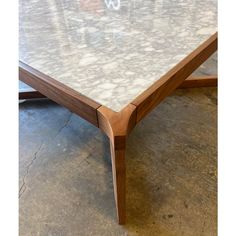 a close up of a table with marble top and wooden legs on concrete flooring