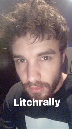 a man with curly hair and beard wearing a black t - shirt looking at the camera