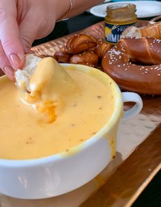 a person dipping cheese into a bowl with pretzels on the table in the background