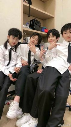 four young men sitting next to each other in front of a book shelf with books