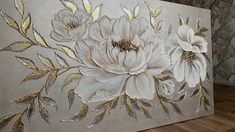 a painting with white flowers and gold leaves painted on the side of a gray wall