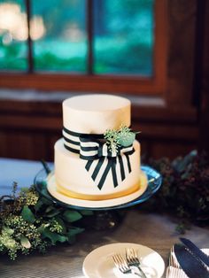 a white and black wedding cake on a table with silverware, greenery and flowers