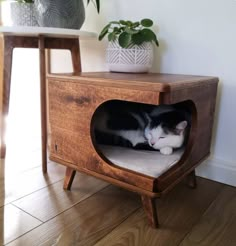 a black and white cat laying in a wooden litter box on top of a table