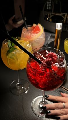 three different types of cocktails on a table with drinks in glasses and one person's hand