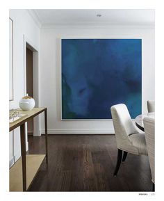 a large blue painting hangs in the corner of a room with two chairs and a table