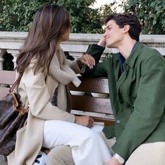 a young man and woman sitting on a bench talking to each other while holding hands