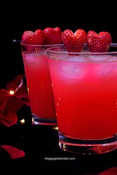 two glasses filled with red liquid and strawberries on the rim, sitting next to each other