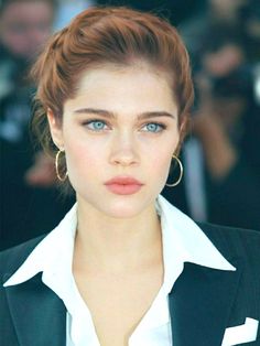 a woman with blue eyes wearing a black jacket and white shirt is looking at the camera