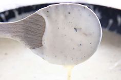 a wooden spoon is pouring sauce into a white bowl with black spots on the surface