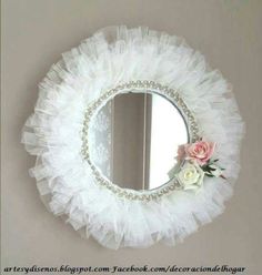 a round mirror hanging on the side of a wall next to a pink rose and white flower