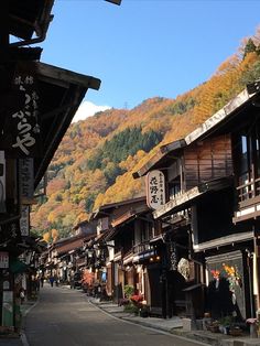 a narrow street with buildings and mountains in the backgrouds, surrounded by autumn foliage