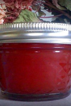 a jar filled with red liquid sitting on top of a white table next to flowers