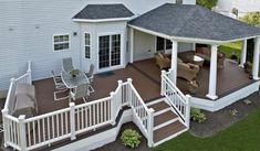 a deck with chairs and table next to a white house on the grass covered yard