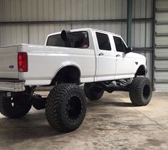 a white pickup truck parked in a garage with large tires on it's flatbed