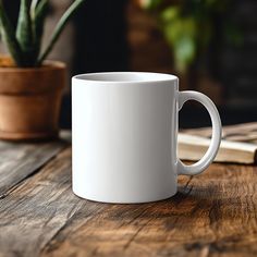 a white coffee mug sitting on top of a wooden table next to a potted plant