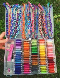 a person holding a box filled with lots of different colored bracelets on top of grass