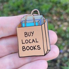 a hand holding a brown paper bag with books on it that says buy local books