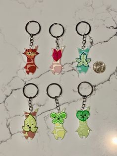 six keychains with different designs on them sitting on a marble counter top next to a coin