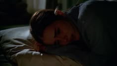 a woman laying on top of a bed under a blanket in the dark with her eyes closed