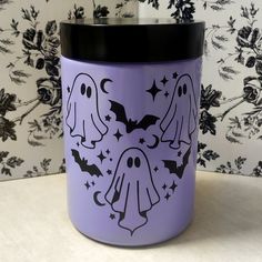 a purple canister with two ghost faces and bats on the side, in front of a wallpapered background